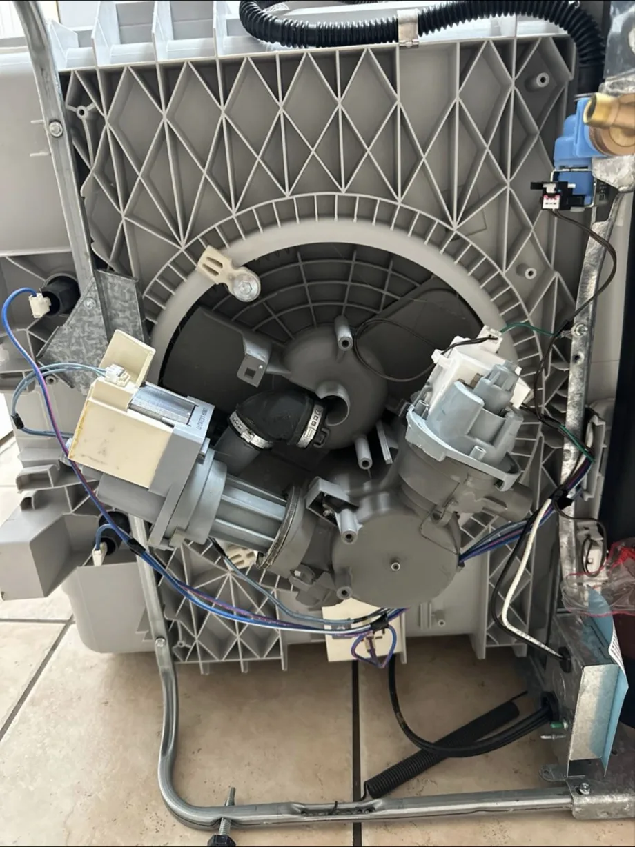 The underside of a dishwasher with pumps, hoses and wiring exposed