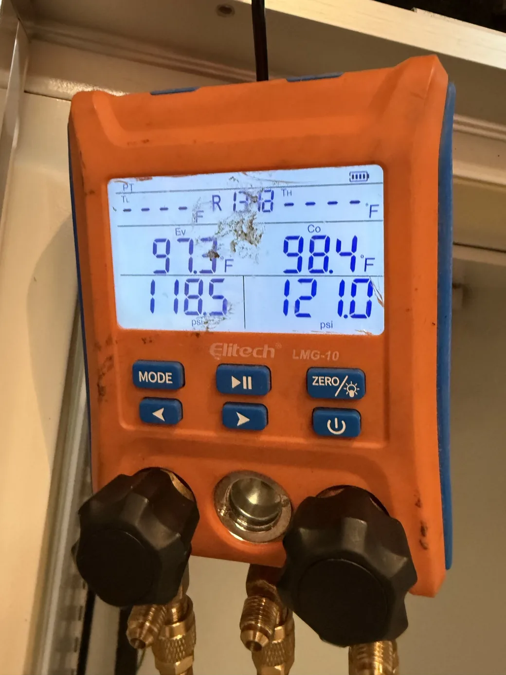 An orange digital refrigeration manifold gauge with its display visible